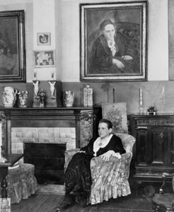 Gertrude Stein (1874-1946) em Paris, França, em março de 1930, sentada em frente a um retrato seu, pintado pelo artista espanhol Pablo Picasso (1881-1973)